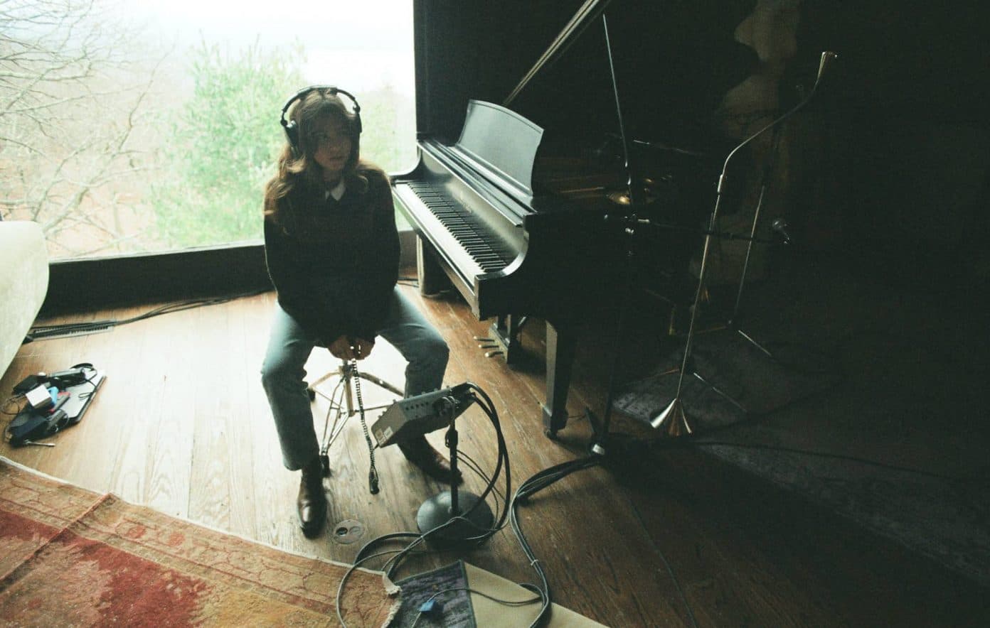 Clairo sitting with headphones near a piano and home recording setup