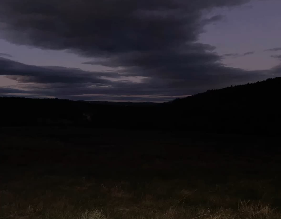 A dark night landscape with heavy clouds over distant hills